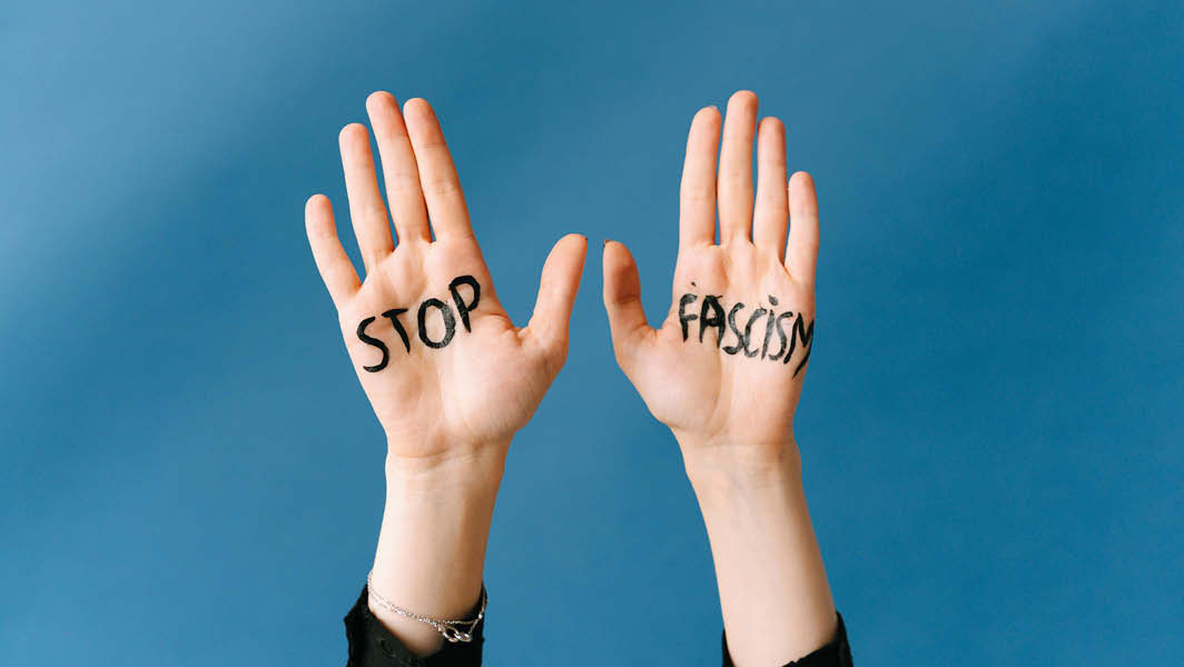 Due mani sollevate su uno sfondo blu con la scritta 'STOP FASCISM' scritta in nero sui palmi delle mani