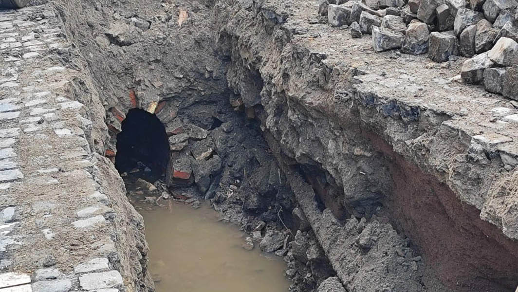 Scavo aperto con una condotta fognaria danneggiata su via Alcide De Gasperi ad Albano Laziale, con presenza di acqua stagnante.