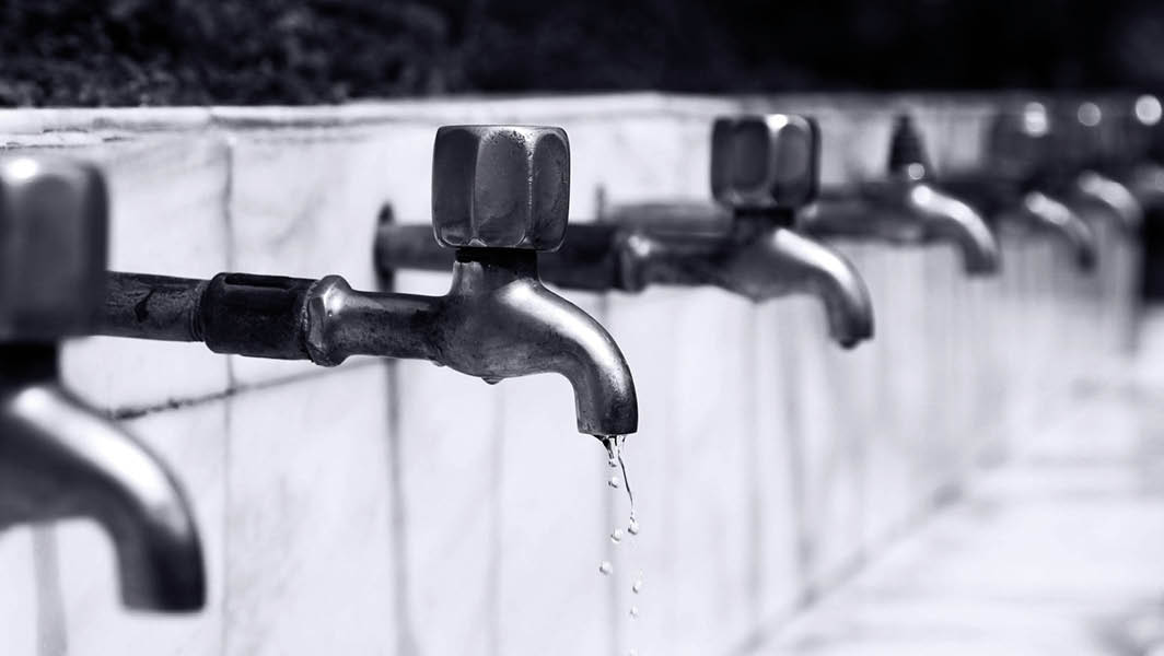 Rubinetti allineati con acqua che gocciola, in bianco e nero, rappresentazione della sospensione idrica nei Castelli Romani.