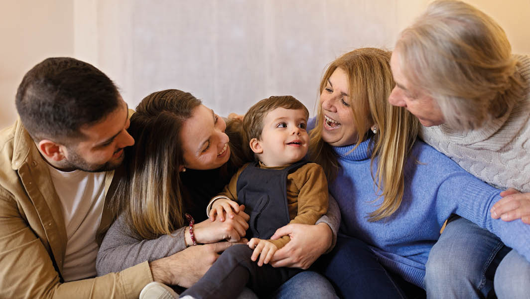 Un gruppo di persone, inclusi adulti e un bambino, sorridono e interagiscono affettuosamente, rappresentando il calore e l'accoglienza che si può trovare in un affido familiare.