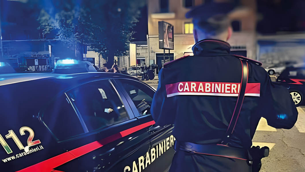 Un carabiniere di spalle accanto a una volante con sirene accese, durante un intervento notturno a Velletri.