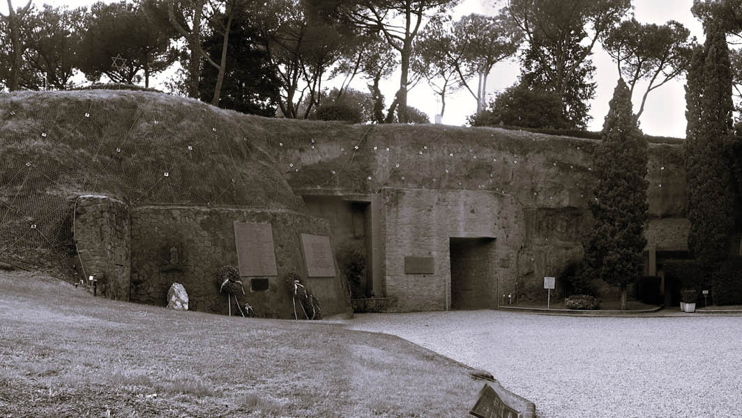 Ingresso del Mausoleo delle Fosse Ardeatine, luogo commemorativo delle 335 vittime dell'eccidio del 1944, con lapidi commemorative e decorazioni floreali.