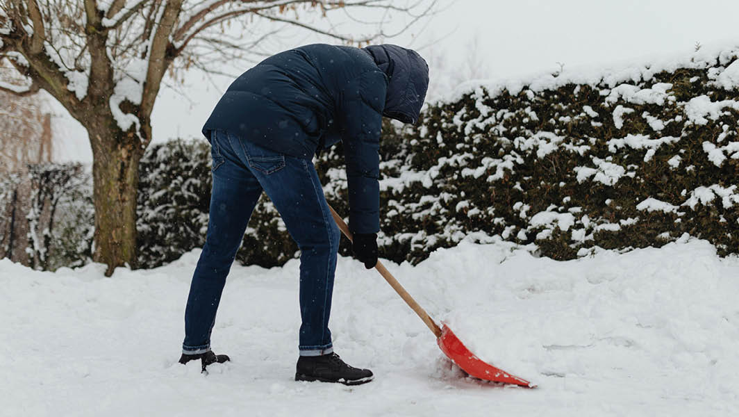 Persona che spalando neve in giardino con una pala rossa durante una nevicata a Rocca Priora.