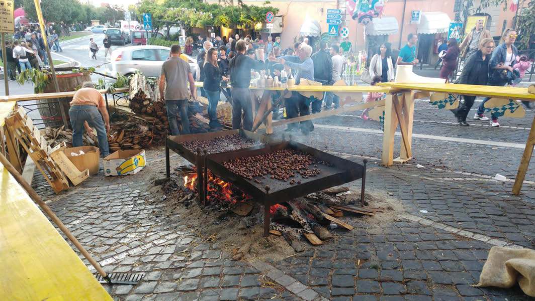 Stand di cottura delle castagne alla brace durante la Sagra delle Castagne a Rocca di Papa, con numerose persone presenti nelle strade del borgo storico.