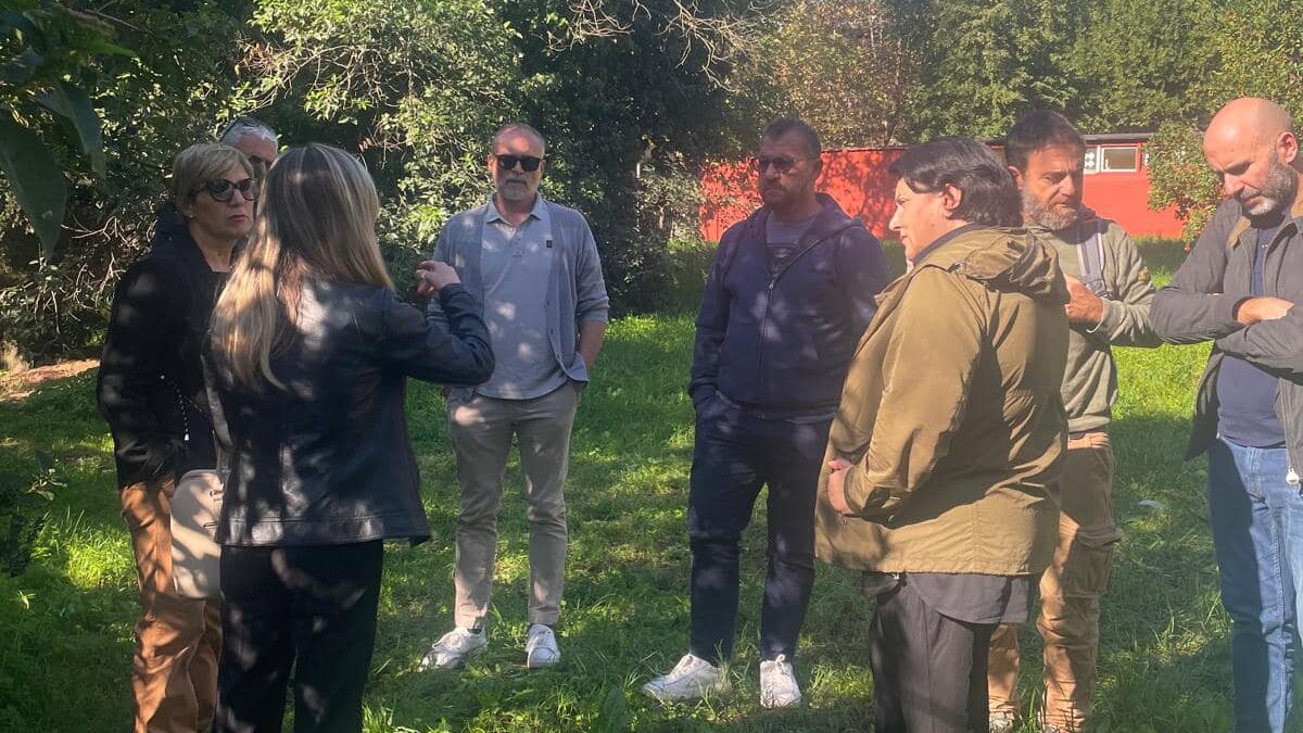 Gruppo di persone, tra cui il sindaco di Albano Laziale e membri del team di progetto, durante un sopralluogo nel cantiere di riqualificazione del Sepolcro degli Orazi e Curiazi, immerso nel verde.