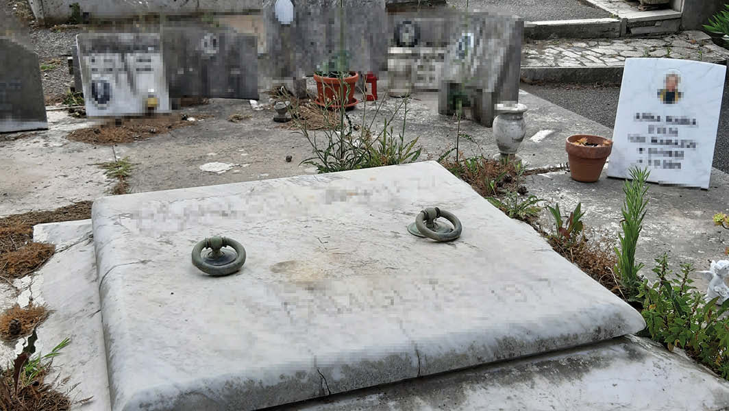 Vista di alcune tombe nel cimitero comunale di Castel Gandolfo, con una lapide in primo piano e altre danneggiate o spostate sullo sfondo.