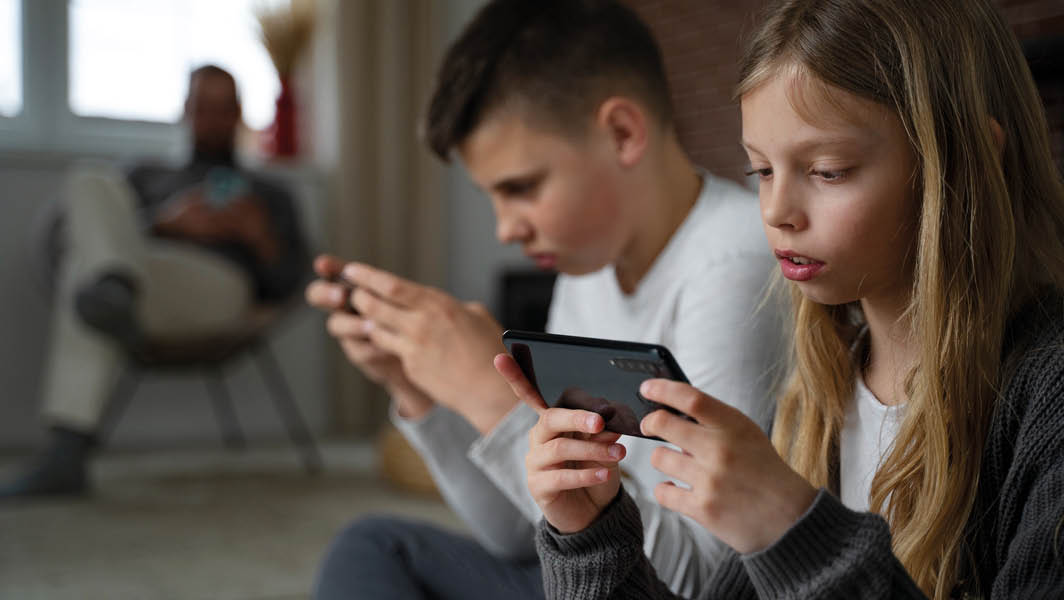 Bambini che utilizzano smartphone con un adulto sullo sfondo, evidenziando i rischi della demenza digitale.