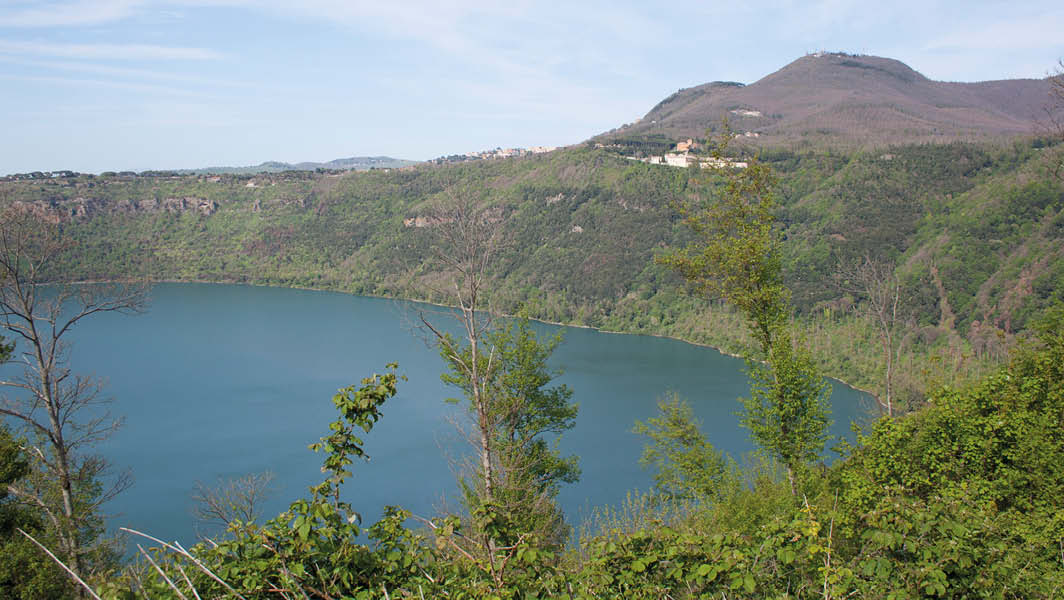 Vista panoramica del Lago Albano circondato da vegetazione e colline dei Castelli Romani.