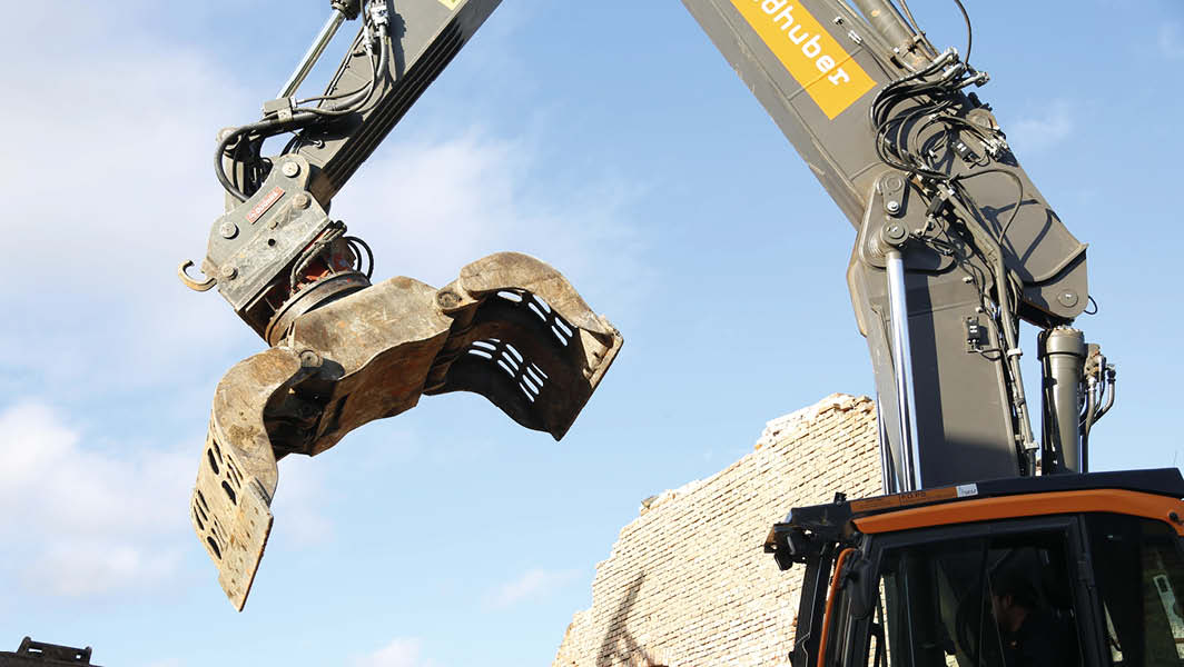 Escavatore in azione durante una demolizione edilizia, con un muro in fase di abbattimento sullo sfondo, simbolo dell'abusivismo edilizio a Marino.