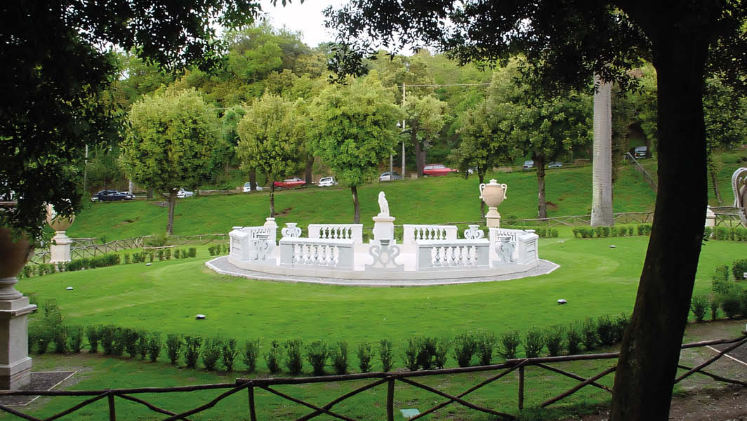 Giardino del parco dell'Ombrellino a Frascati, con una fontana centrale circondata da un prato verde e decorazioni in marmo.