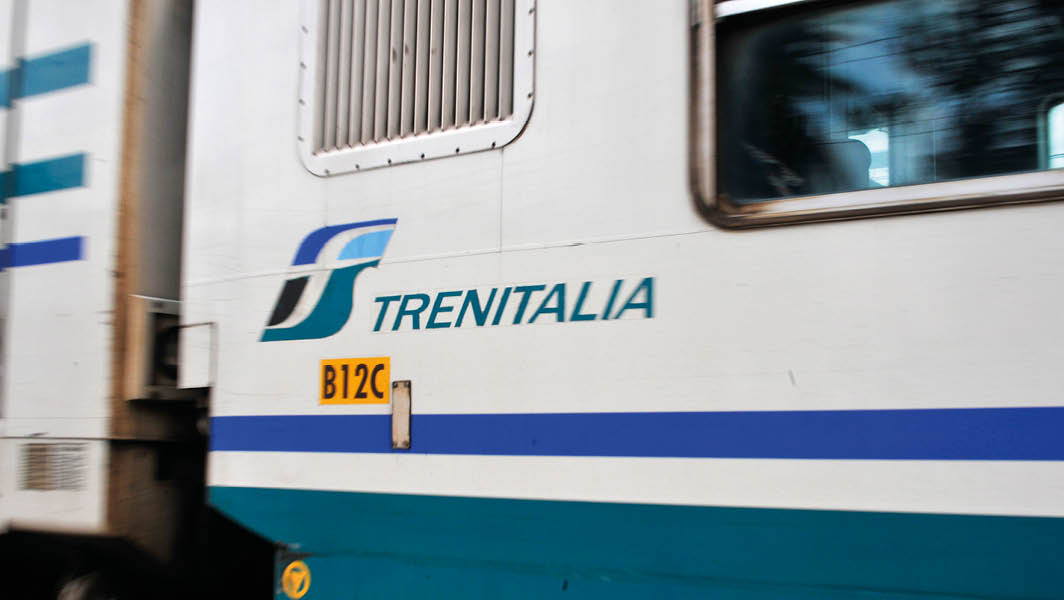 Primo piano di un treno Trenitalia in movimento, con logo visibile sulla fiancata.