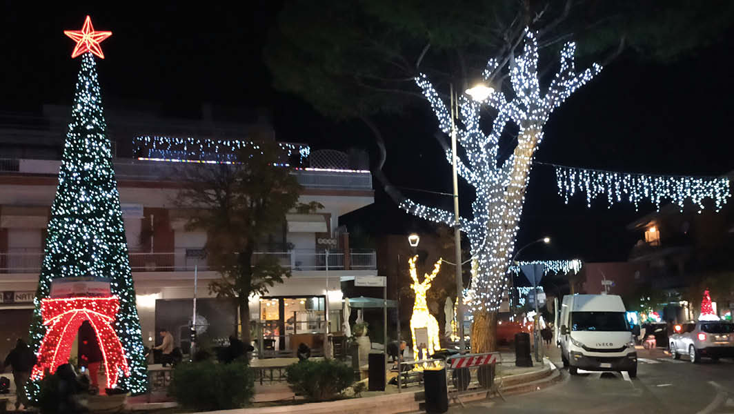 Decorazioni natalizie a Santa Maria delle Mole: un albero illuminato con luci colorate e una renna luminosa accanto, in una piazza decorata per il Natale.