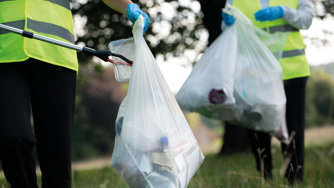 Operatori ecologici Tekneko in azione a Monte Compatri raccolgono rifiuti in un ambiente naturale, indossando gilet riflettenti e guanti protettivi.