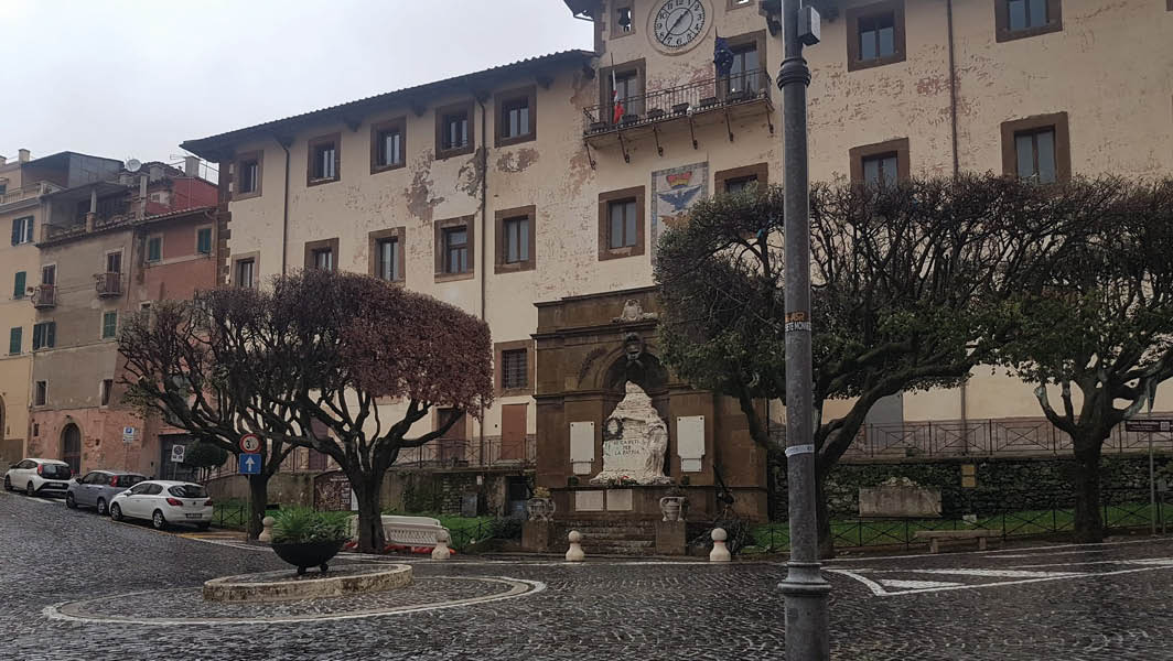 Vista della piazza Marco Mastrofini a Monte Compatri, con i lecci potati e il Monumento ai Caduti davanti al Palazzo Comunale.