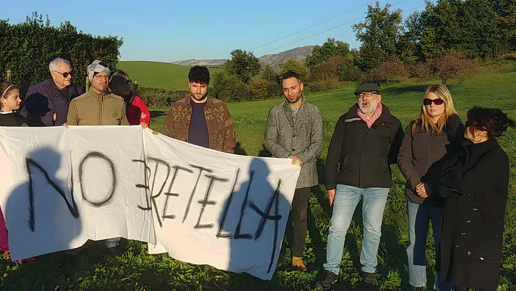 Gruppo di cittadini a Casale Malatesta, Velletri, con striscione contro la bretella Cisterna-Valmontone in un campo verde.