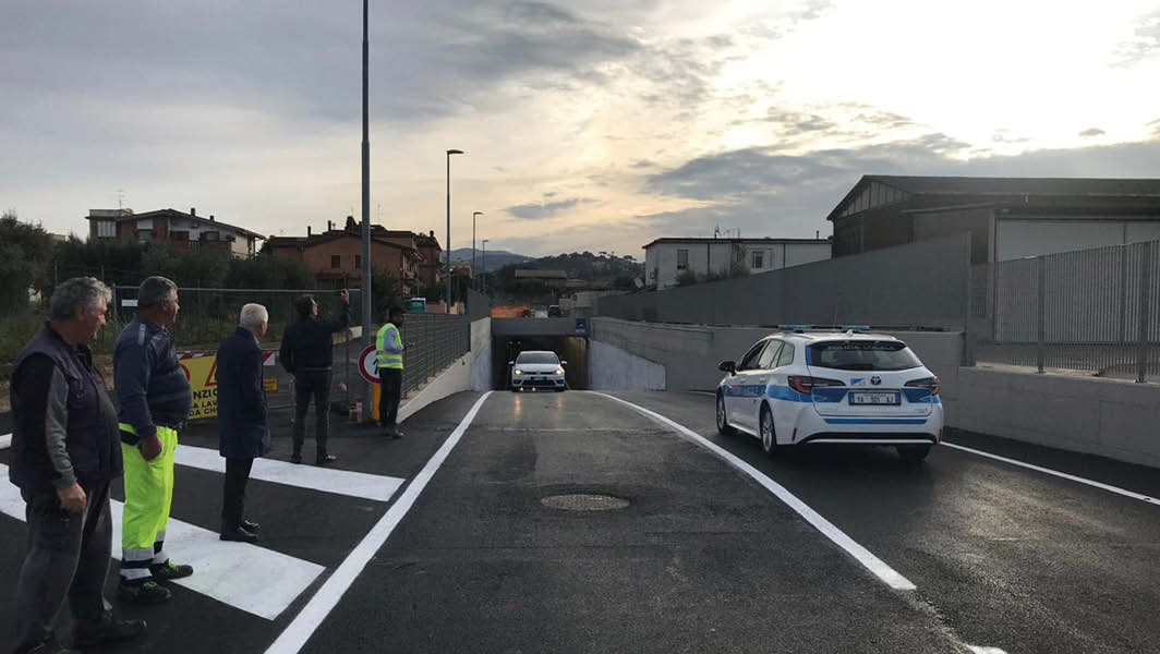 Sottopasso ferroviario di Pavona ad Albano Laziale, con auto e persone che ispezionano la strada appena completata, durante un tramonto.