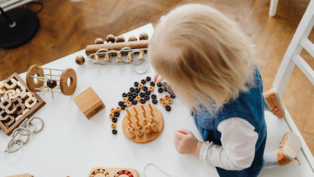 Un bambino piccolo seduto a un tavolo gioca con giochi educativi in legno, tipici di un ambiente di asilo nido come quelli di Rocca Priora.