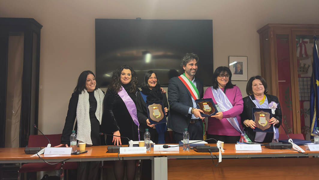 Gruppo di persone sorridenti, tra cui il sindaco con fascia tricolore, che mostrano targhe celebrative durante la cerimonia di Grottaferrata Capitale di Costruiamo Gentilezza 2025.