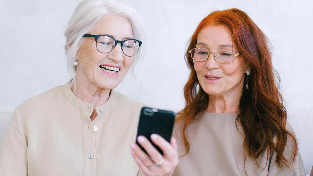 Due donne anziane sorridenti che guardano uno smartphone insieme, simbolo di apprendimento digitale e inclusione tecnologica dopo il corso a Lariano.