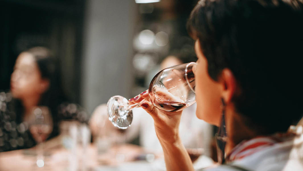 Una donna degusta un calice di vino rosso durante il Festival delle tradizioni e delle eccellenze a Lanuvio, con altre persone sullo sfondo.