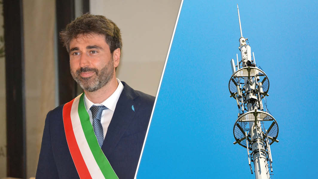 Il sindaco di Grottaferrata Mirko Di Bernardo con fascia tricolore accanto a un’antenna di telecomunicazioni, simbolo del Piano Antenne del Comune.