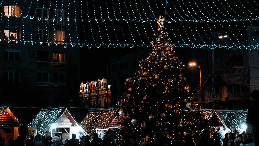 Un albero di Natale illuminato al centro di una piazza, circondato da bancarelle natalizie e luminarie scintillanti in una notte festiva a Velletri.