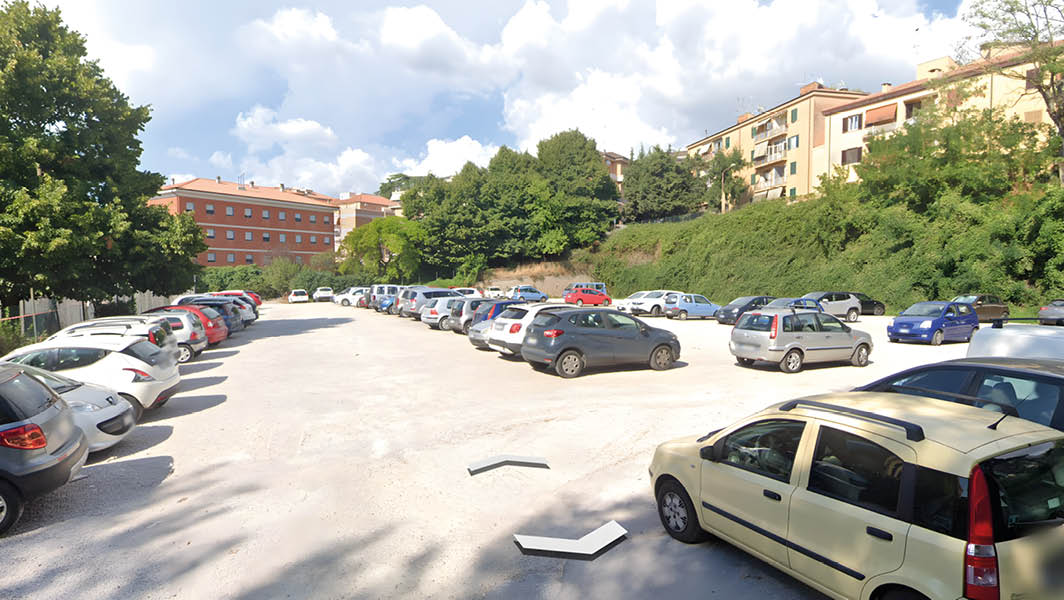 Parcheggio sterrato adiacente alla scuola Collodi ad Albano Laziale, con diverse automobili parcheggiate, circondato da edifici residenziali e aree verdi.