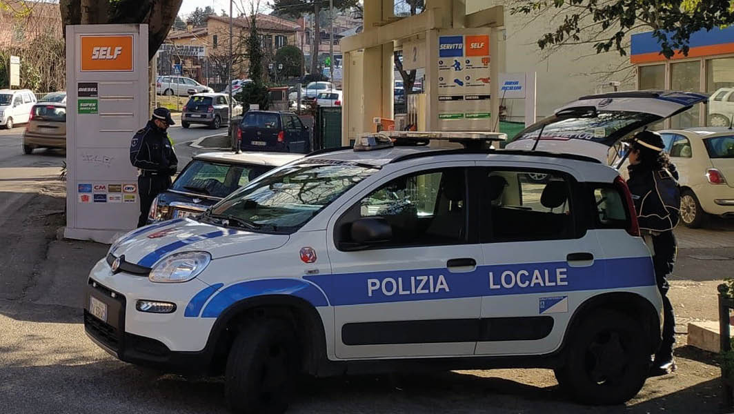 Auto della Polizia Locale di Grottaferrata parcheggiata presso una stazione di servizio, con un agente in divisa che svolge attività di controllo.