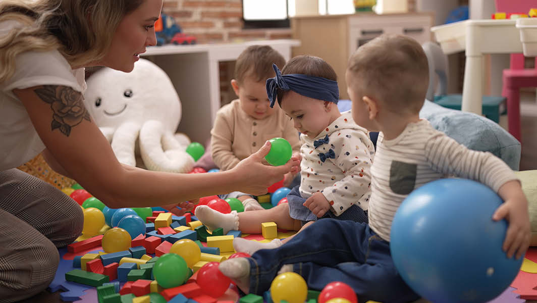 Educatrice gioca con bambini piccoli in un asilo nido a Rocca di Papa, circondati da palline colorate e giochi educativi.