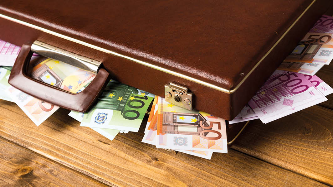 Valigetta marrone con banconote di euro che fuoriescono, simbolo degli sprechi nella pubblica amministrazione.