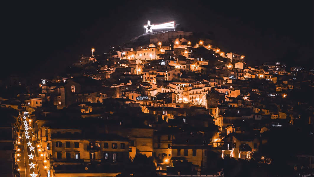 Vista notturna di Rocca di Papa illuminata per il Natale con la grande Stella simbolo delle festività brillando sulla Fortezza medievale.