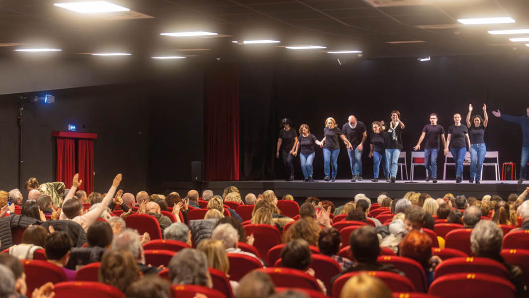 Un gruppo di attori saluta il pubblico con un inchino sul palco del Teatro Vittoria Colonna di Marino, mentre la platea applaude calorosamente.