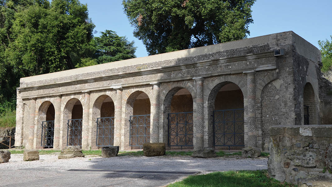 Antico edificio del Santuario di Giunone Sospita a Lanuvio, circondato da alberi e resti archeologici.