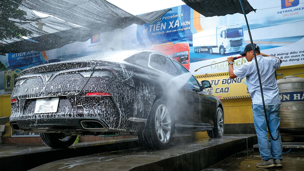 Un autolavaggio a Velletri con un lavoratore che lava un'auto nera utilizzando un getto d'acqua ad alta pressione.