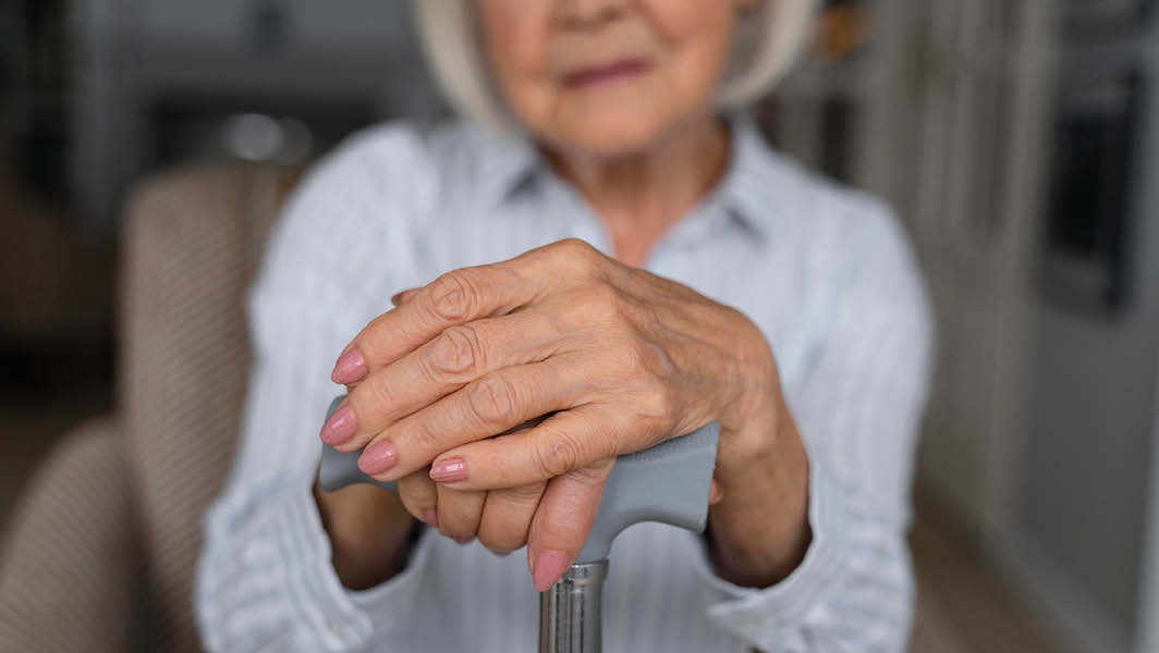 Primo piano di una donna anziana che appoggia le mani su un bastone, simbolo della vita quotidiana degli anziani a Velletri.